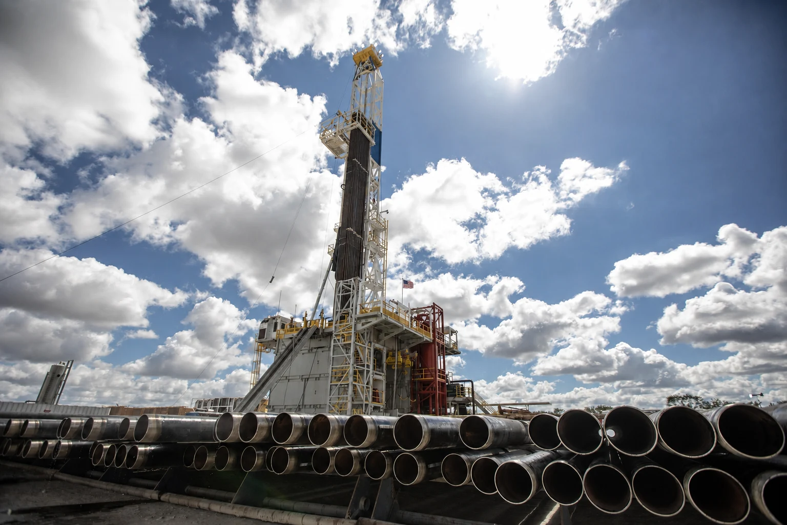Drilling rig behind rows of steel pipe beneath a blue sky